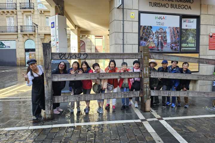 Group of people posing behind a wooden fence in front of a tourist office on a wet street.