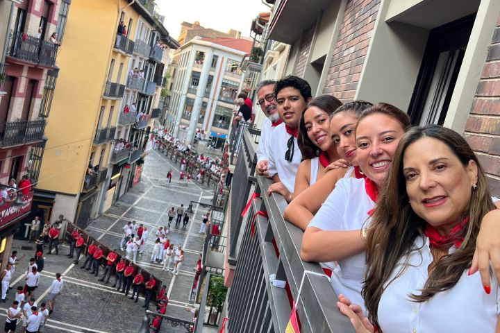 People in white shirts with red scarves on a balcony watching a street festival.