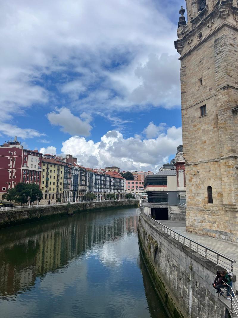 River with colorful buildings and a stone tower under a cloudy sky.
