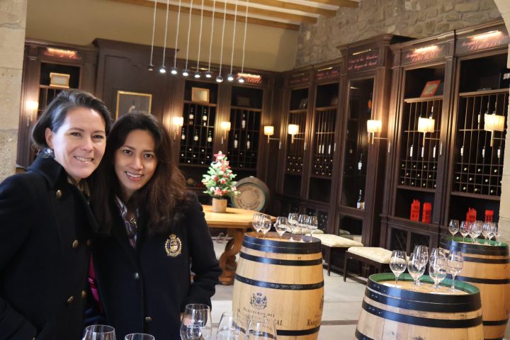 Two people smiling in a wine tasting room with barrels and glasses.