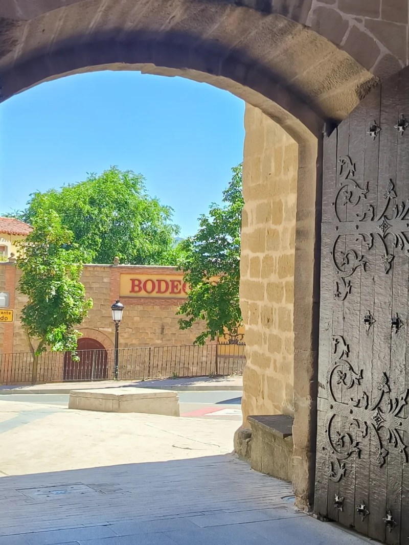 View through open archway to street and building with 'BODEGA' sign.