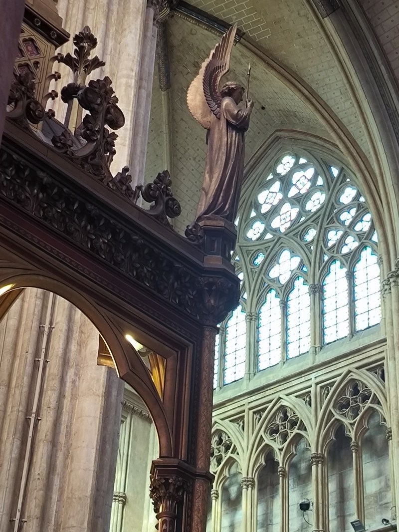 Interior of a cathedral with angel statue and ornate columns, stained glass windows in background.
