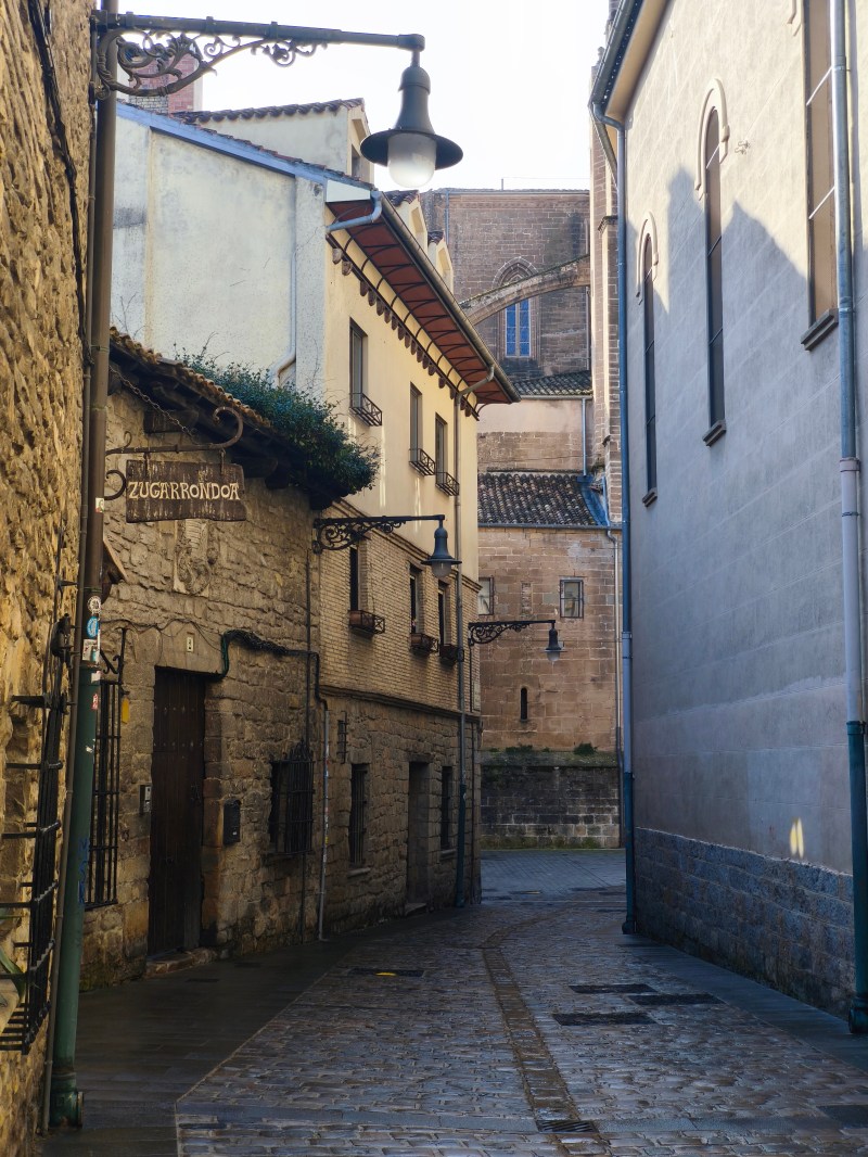 Narrow cobblestone alley with stone buildings and a hanging street lamp.