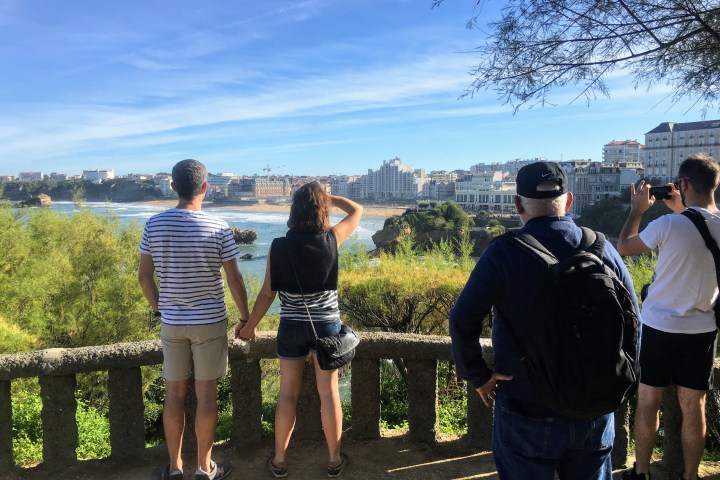 Four people overlooking a coastal cityscape under a clear blue sky.