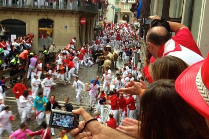 Crowd running from bulls on a narrow street during a festival.