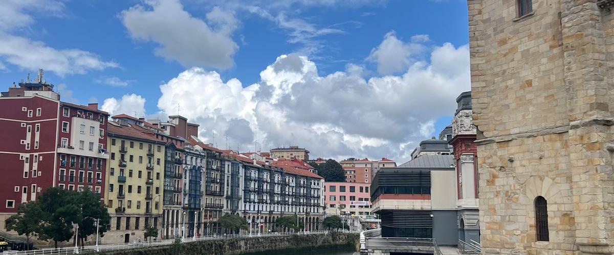 River with colorful buildings and a stone tower under a cloudy sky.