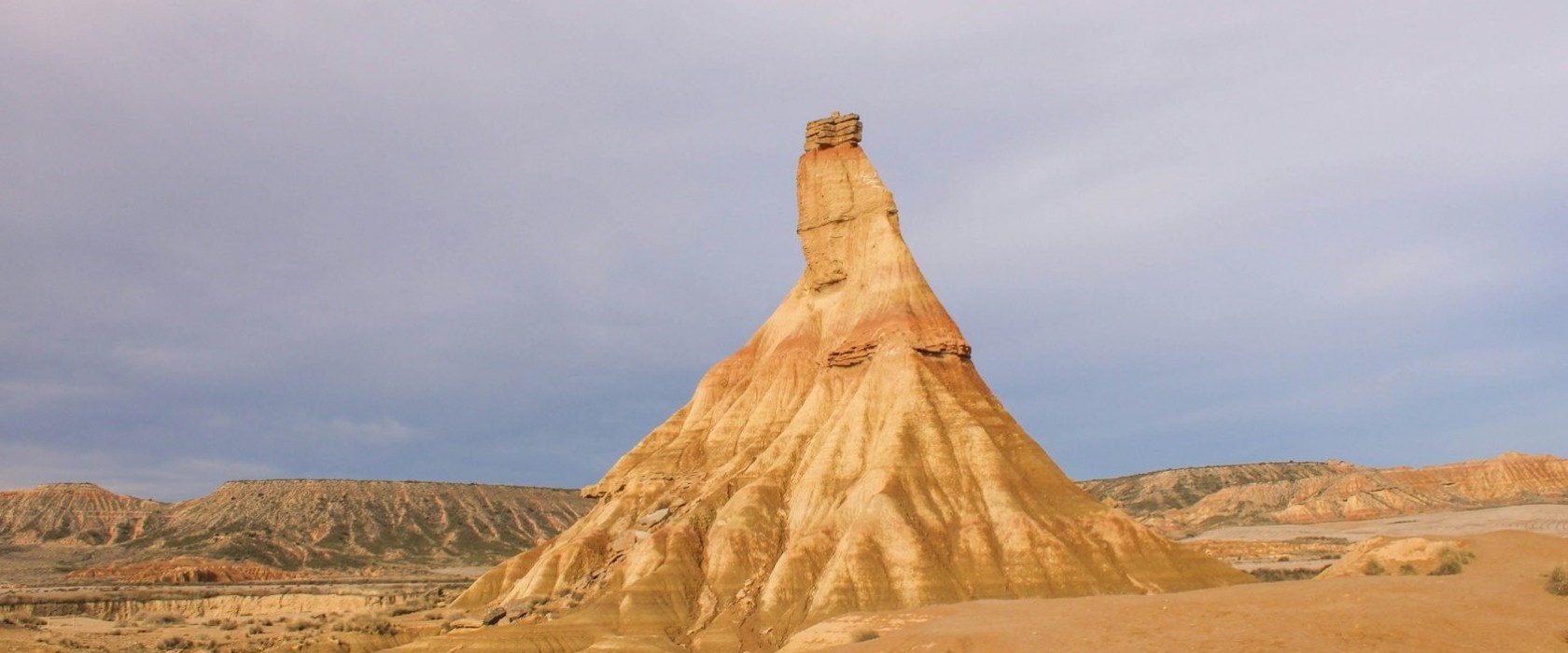 Eroded rock formation in a desert landscape under cloudy sky.