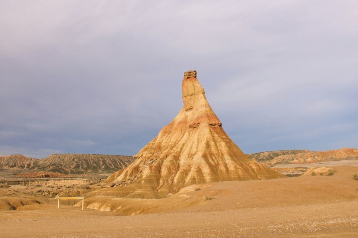Eroded rock formation in a desert landscape under cloudy sky.