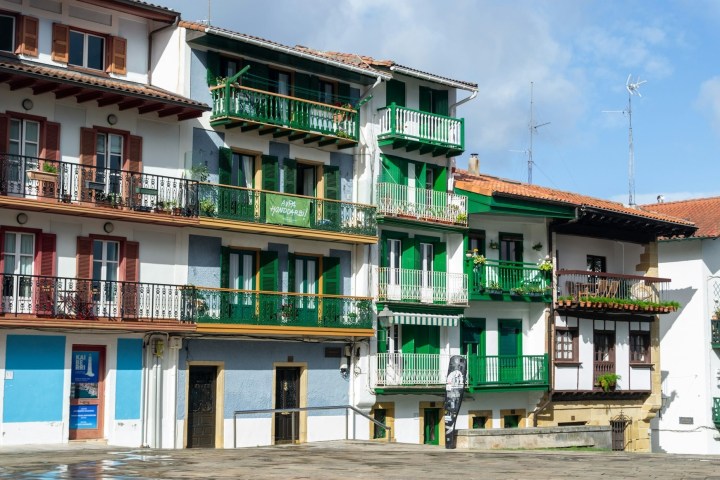 Colorful buildings with green balconies in a sunlit plaza.