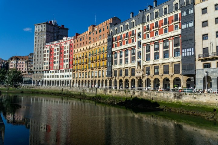 Colorful buildings reflected in calm river under clear blue sky.