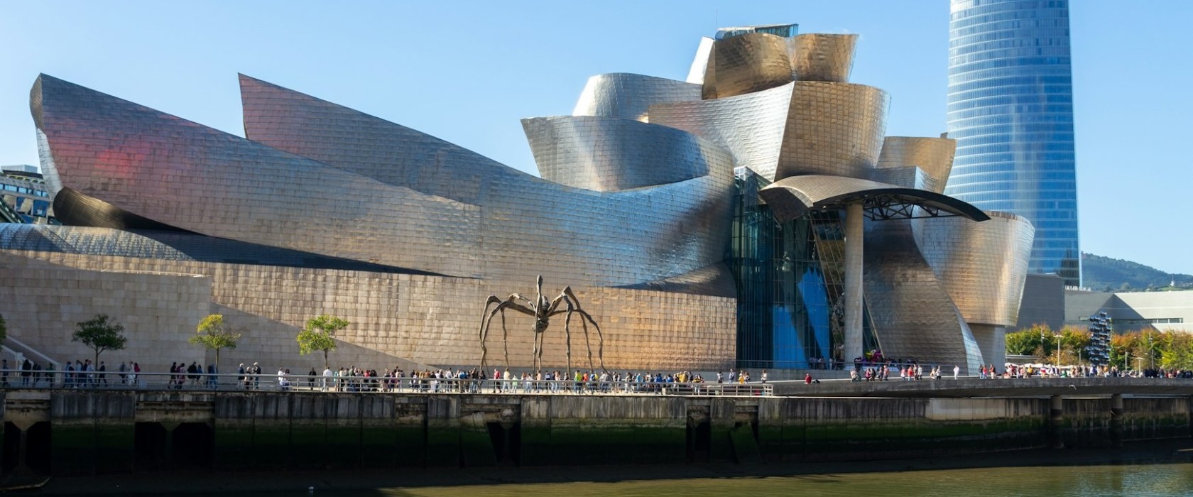 Guggenheim Museum Bilbao with a spider sculpture and river in foreground.