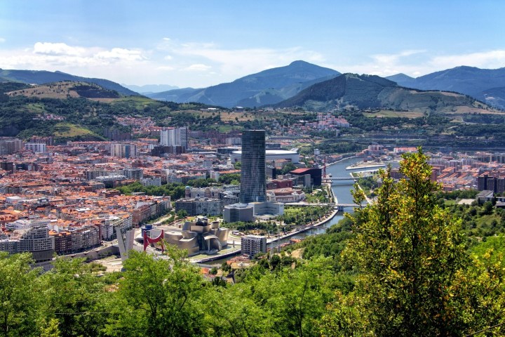 Cityscape with river, tall tower, and hills in the background.