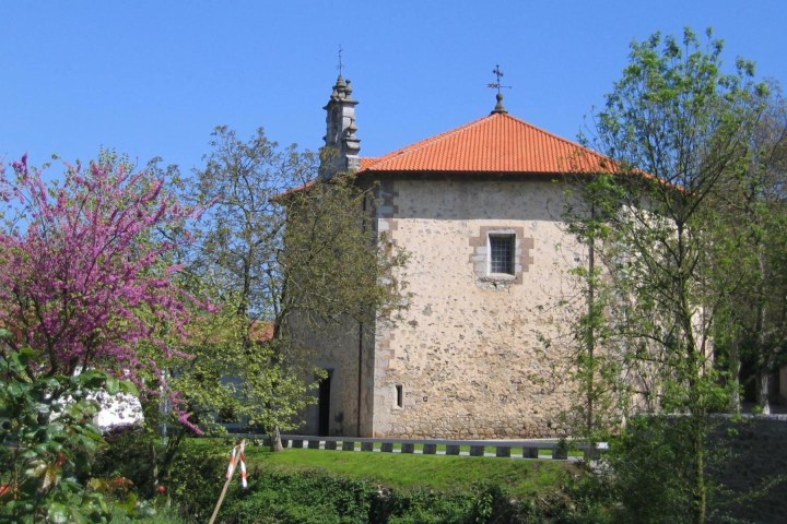 Small stone church with red roof, surrounded by trees.