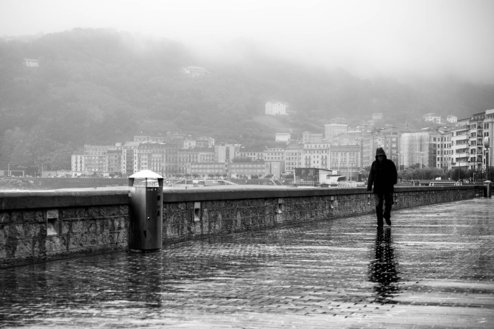 Person walking on wet promenade by city in foggy weather.