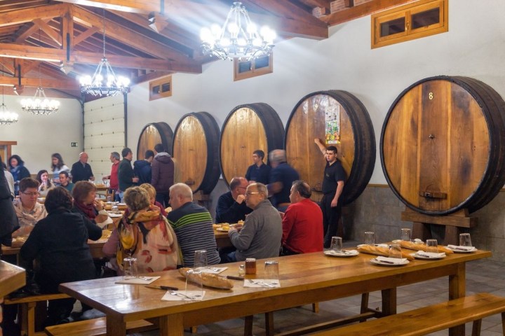 People dining in a room with large wooden barrels and long tables.